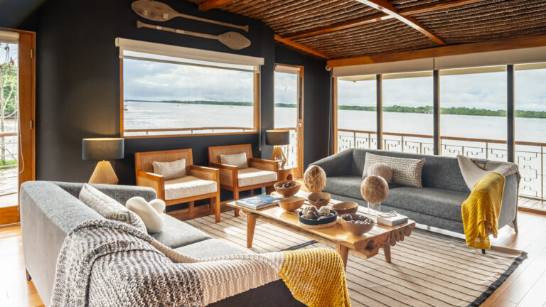 Riverboat interior with two couches with small throw blankets and two small chairs, large windows and an open feel