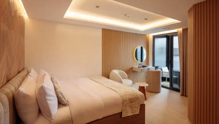 Single Suite with queen bed on Hermes mega-catamaran with white linens, wood accent walls, recessed lighting & private balcony.