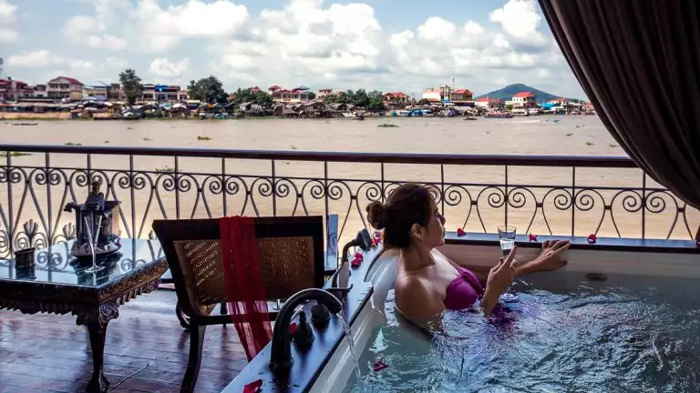 Women laying in luxury bath tub on the balcony of her room aboard a small river boat overlooking the river.