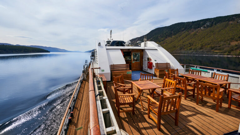 exterior of small ship cruise lord of the glens cruising through a calm passage way with trees on both sides