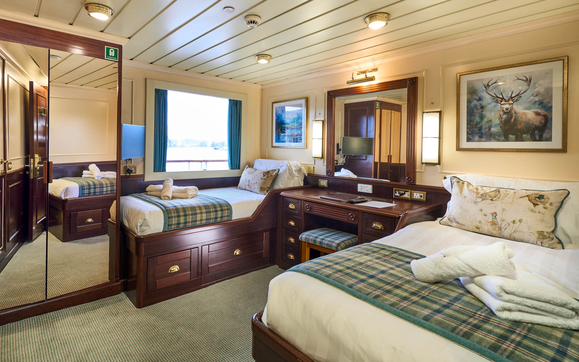 bedroom aboard small cruise ship, with two beds with folded towels and a picture window.