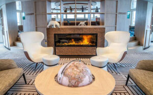 2 modern, white, wingback chairs sit beside a globe & fireplace aboard Nat Geo Endurance & Resolution ships.