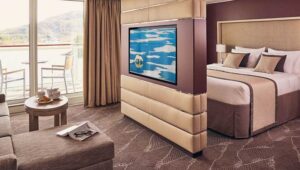 Balcony Suite with double bed, couch, desk, chair, and private balcony with table and chairs aboard National Geographic Endurance polar expedition ship.