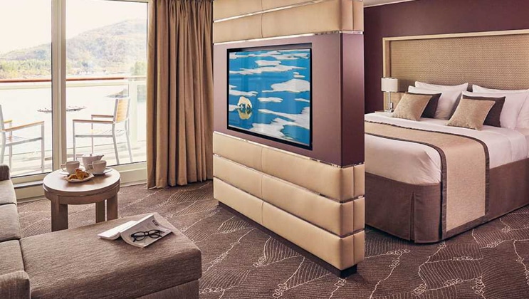 Balcony Suite with double bed, couch, desk, chair, and private balcony with table and chairs aboard National Geographic Endurance polar expedition ship.