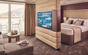 Balcony Suite with double bed, couch, desk, chair, and private balcony with table and chairs aboard National Geographic Endurance polar expedition ship.