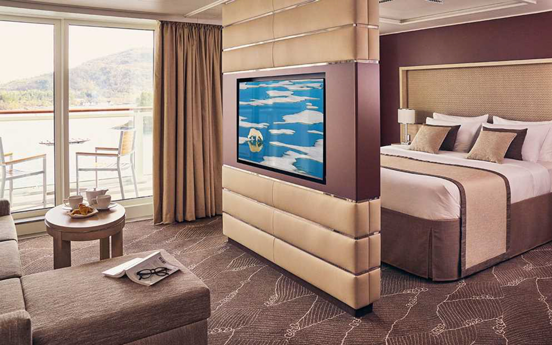 Balcony Suite with double bed, couch, desk, chair, and private balcony with table and chairs aboard National Geographic Endurance polar expedition ship.