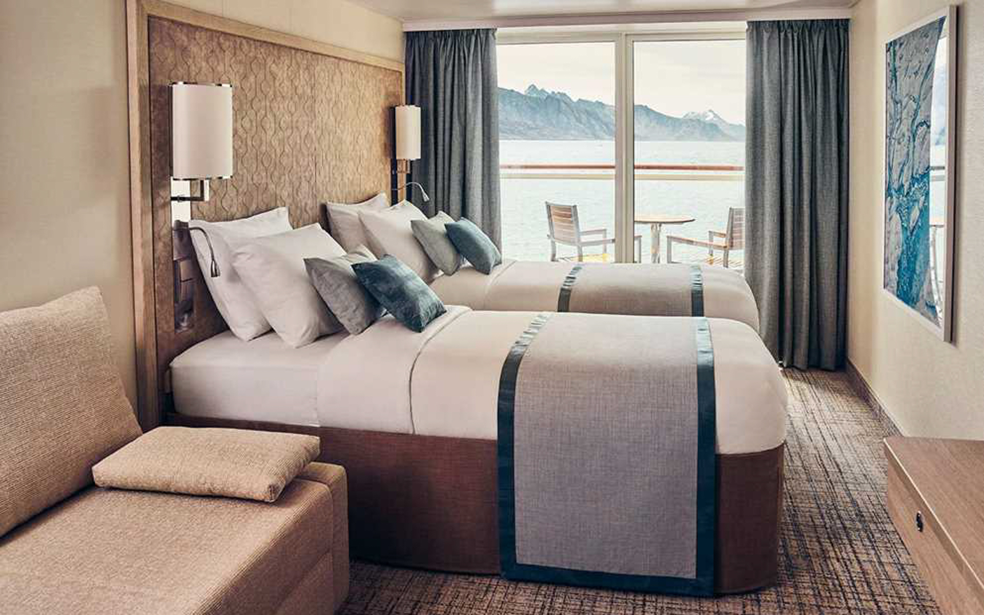 Double beds in a light wood cabin with balcony a table and two chairs aboard National Geographic Endurance & Resolution