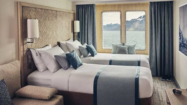 Two single beds in a light colored wooded cabin. Featuring a sofa, window alcove seating and a closet with ample storage.