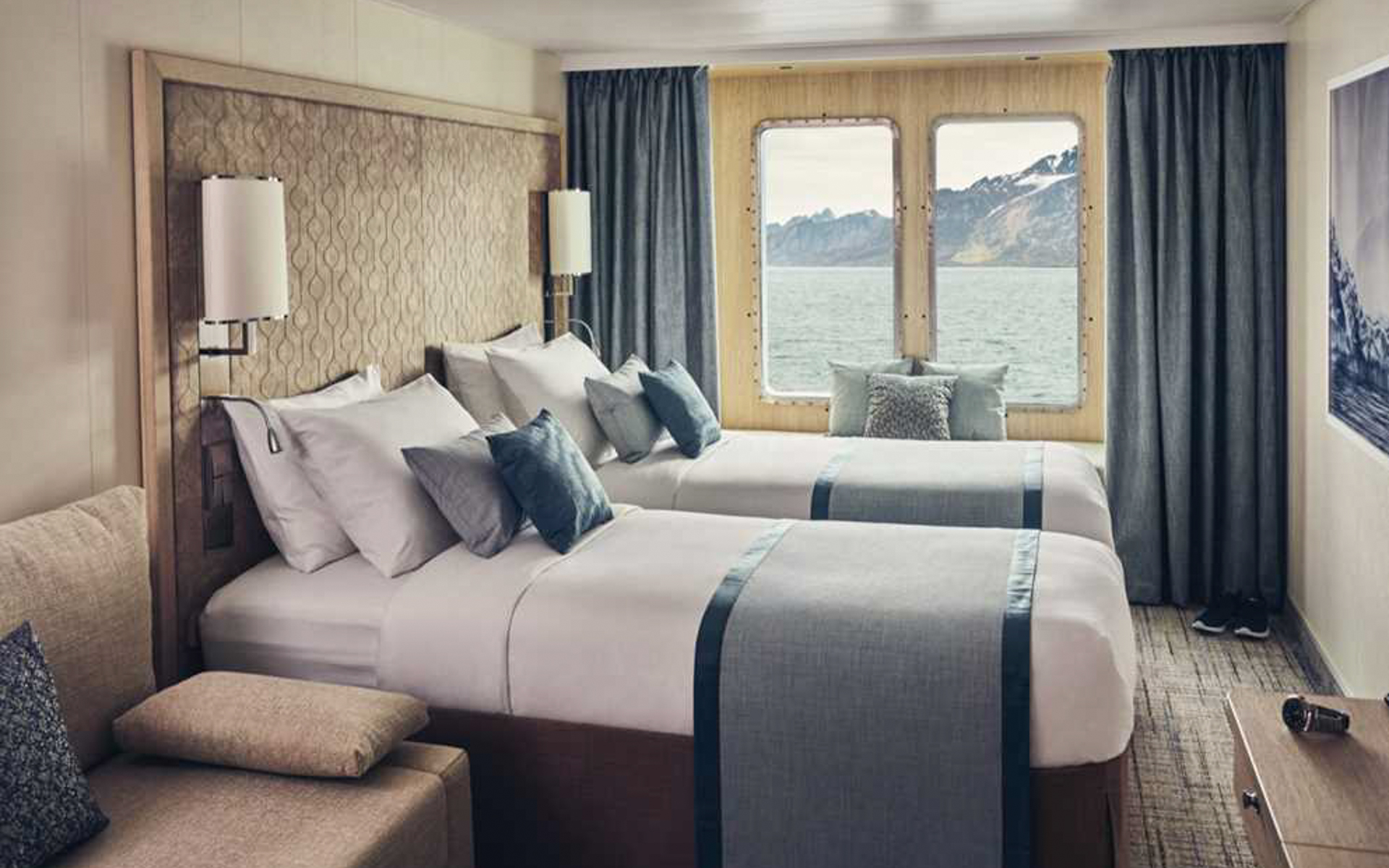 Two single beds in a light colored wooded cabin. Featuring a sofa, window alcove seating and a closet with ample storage.
