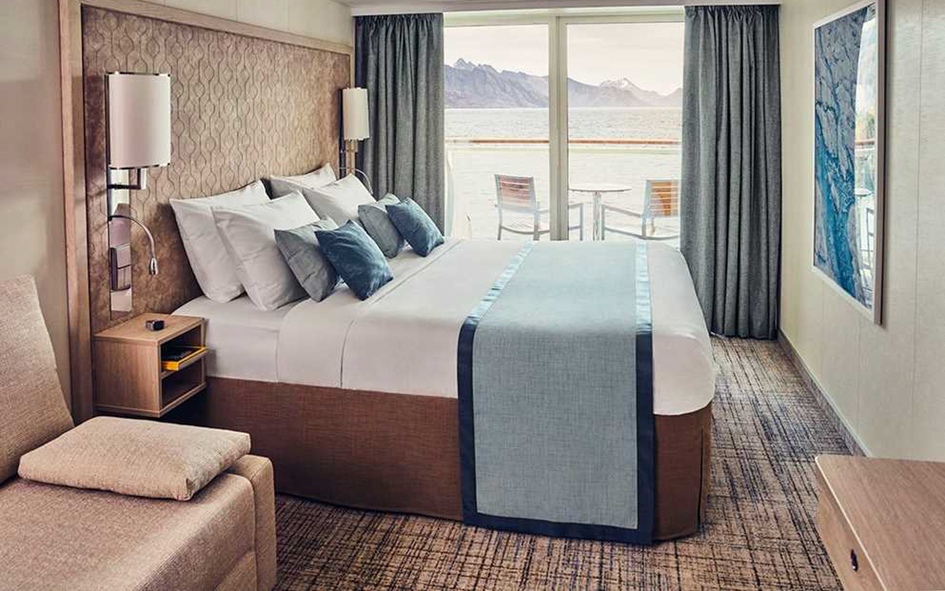 Double beds in a light wood cabin with balcony a table and two chairs aboard National Geographic Endurance & Resolution.