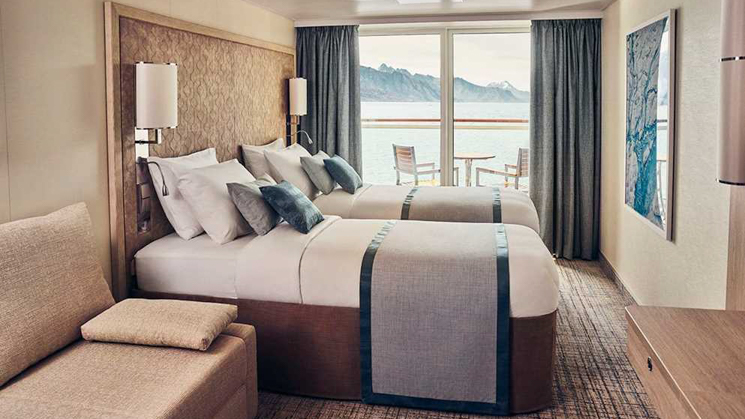 Double beds in a light wood cabin with balcony a table and two chairs aboard National Geographic Endurance & Resolution