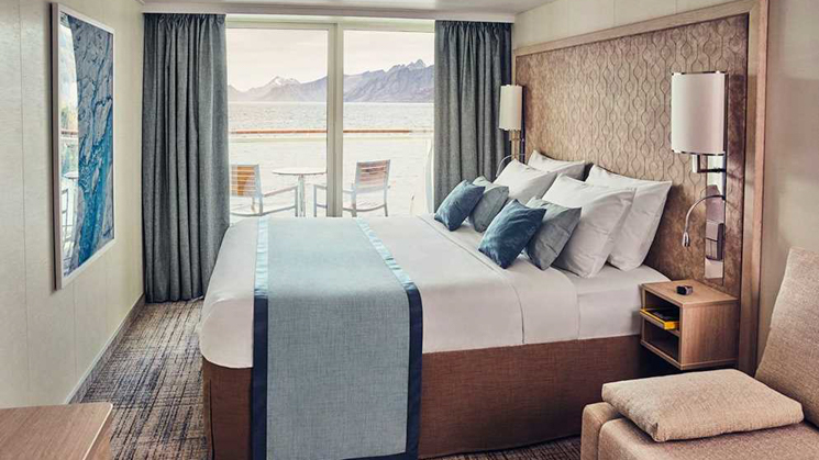 Nat Geo resolution cabin with balcony, a table and two chairs with a comfortable double bed where you can view the Antarctica