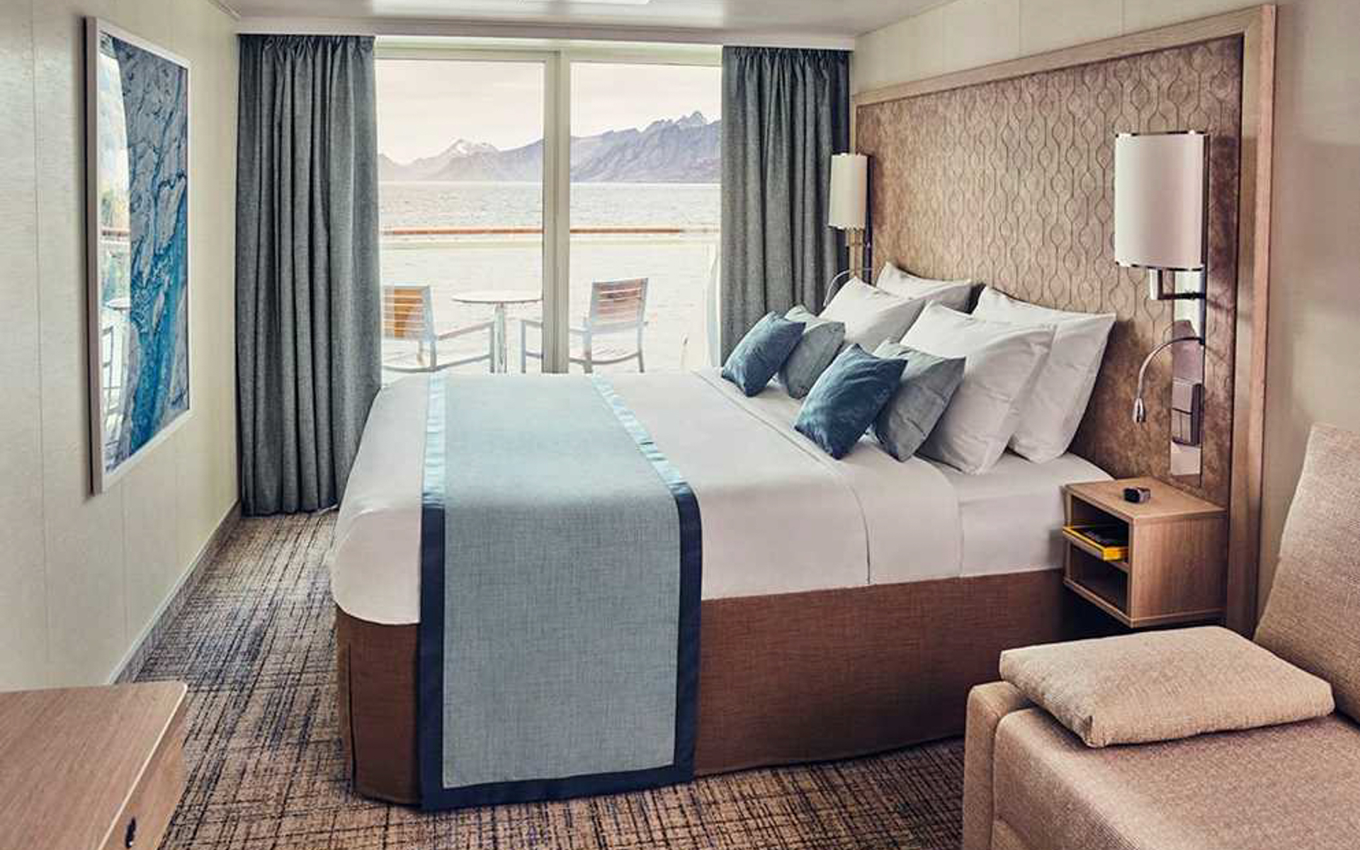 Double bed in a light wood cabin with balcony a table and two chairs aboard National Geographic Endurance & Resolution