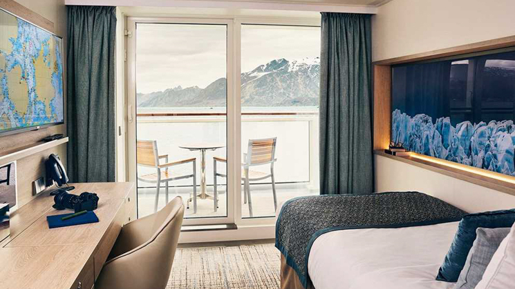 Featuring a single bed with a balcony that has a table and two chairs. A writing desk with a leather chair with a regional map