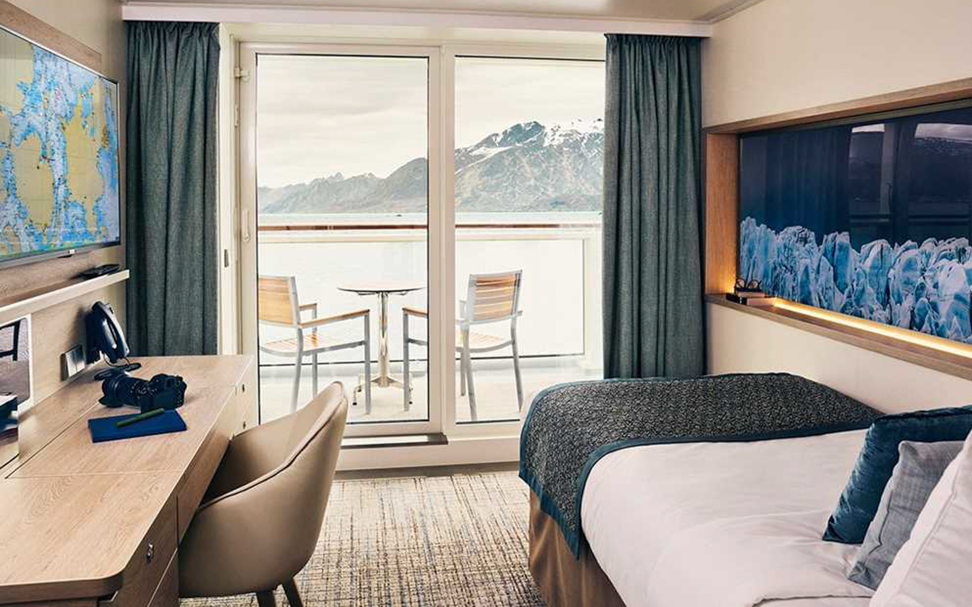 Featuring a single bed with a balcony that has a table and two chairs. A writing desk with a leather chair with a regional map