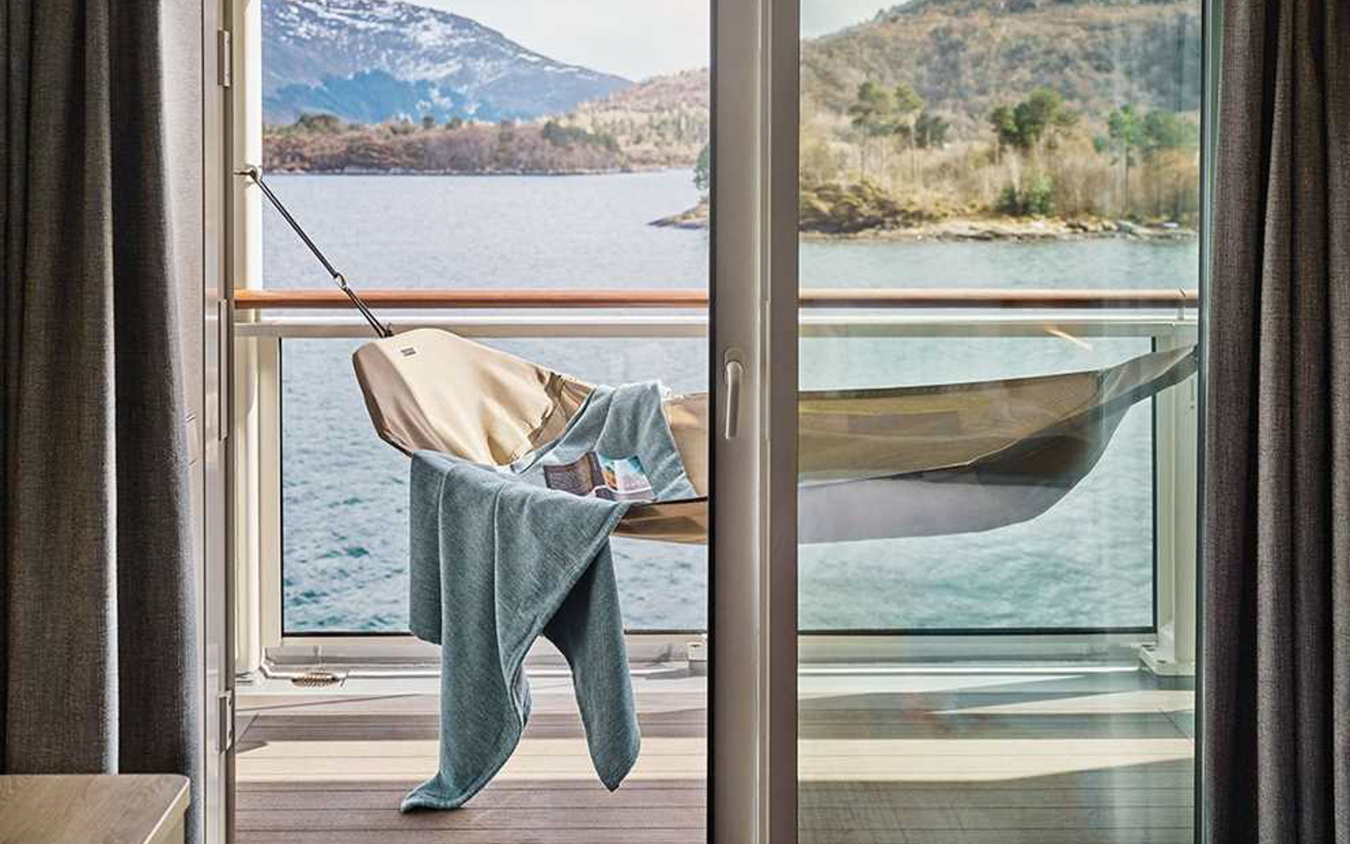 empty beige hammock with blue blanket sits in sunlight on private cabin balcony of Nat Geo Resolution & Endurance ships.
