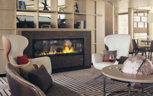 2 modern, white wingback chairs sit empty beside a coffee table with globe in front of a gas fireplace on Nat Geo Endurance.