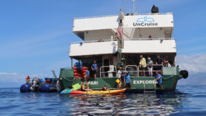 Exterior of Safari Explorer ship with green hull, 2 white upper decks & large aft platform where kayakers pull alongside.