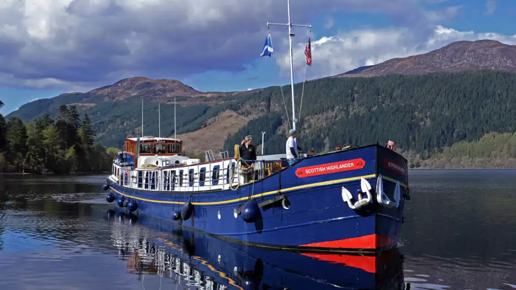 Scottish Highlander hotel barge sitting still in calm water with red-&-blue exterior & on a sunny day in Scotland.