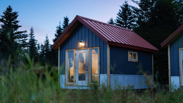 Cabin at dusk at Bear Camp Alaska with a red roof, large windows with a glass door