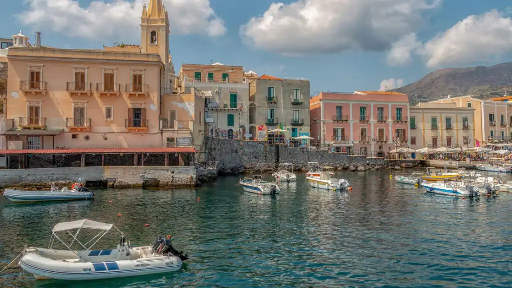 Quiet harbor with small fishing boats & dinghies lined by colorful Mediterranean buildings on a sunny day in Italy.
