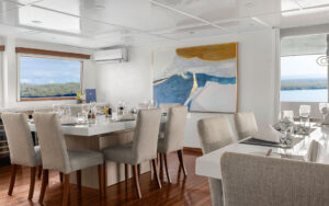 National Geographic Delfina ship's dining room with wood floors, white walls & chairs, & glass tables in open concept.