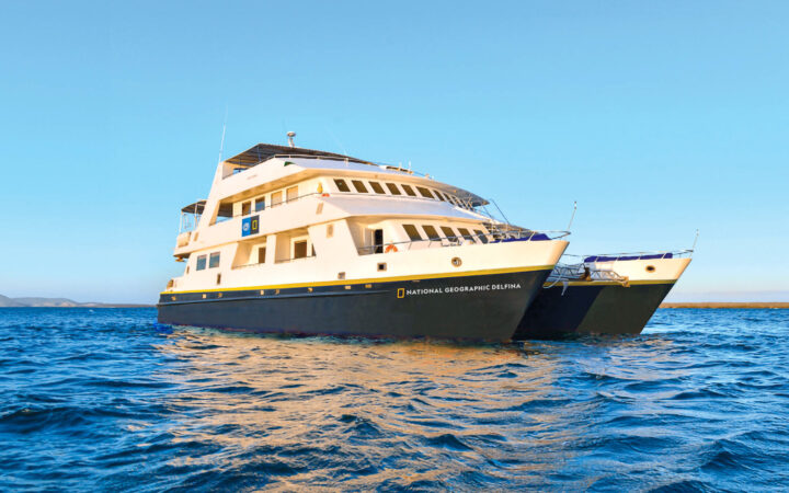 Luxury catamaran National Geographic Delfina. Colored white with a royal blue hull floats in the Galapagos on a blue sunny day