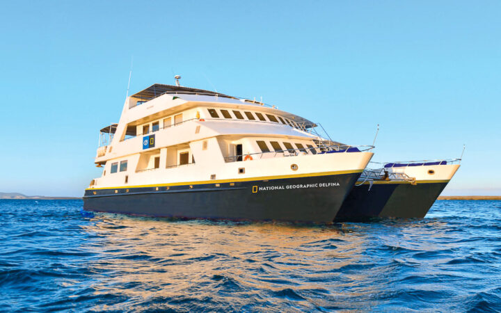 Luxury catamaran National Geographic Delfina. Colored white with a royal blue hull floats in the Galapagos on a blue sunny day