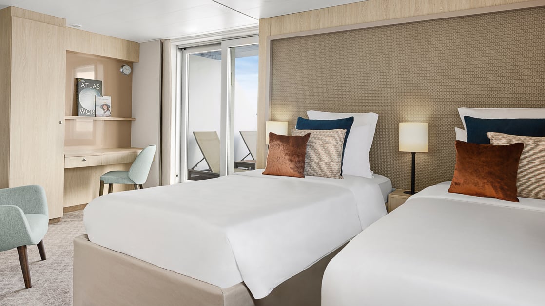 Floor to ceiling glass door to balcony with single bed of white bedding, seating area with table, vanity desk and mirror.