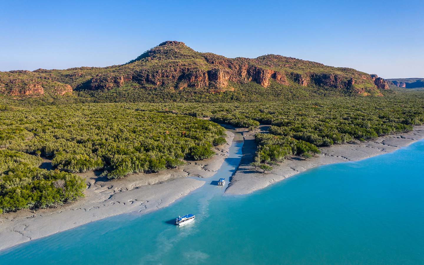 Two small Australia cruise ships seen from above sailing into the Hunter River in the remote Kimberley with green trees and blue water