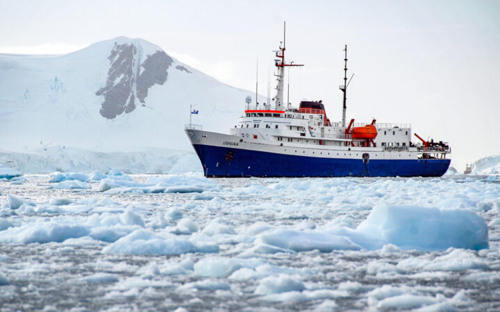 Ushuaia expedition ship port side sailing through icebergs with mountain in background.