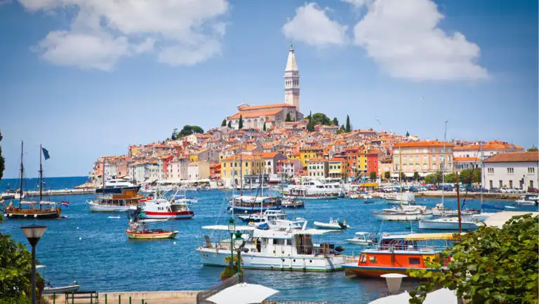 Busy Mediterranean harbor with yachts & fishing boats in blue sea by terracotta-roofed beige stone buildings in the Adriatic.