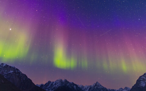 Northern Lights in green, pink & purple shine above jagged peaks during the Arctic Golden Autumn expedition cruise.