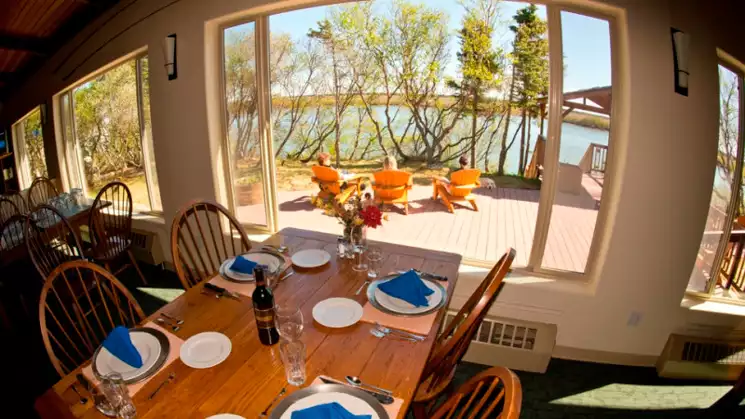 Rustic dining table set inside King Salmon Lodge white plates with blue napkins looking out through the large picture windows on a sunny day