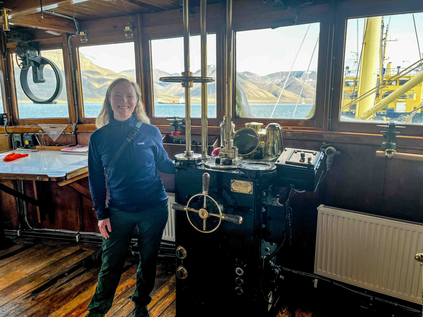 Woman in blue sweater & green pants stands on bridge of MS Stockholm ship in Svalbard.