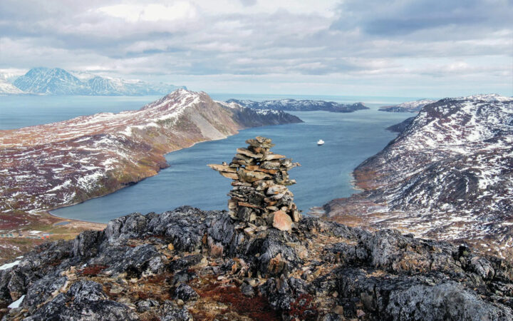 Stacked rocks on the top of am overlook looking down into the bay of water with a small ship off in the distance