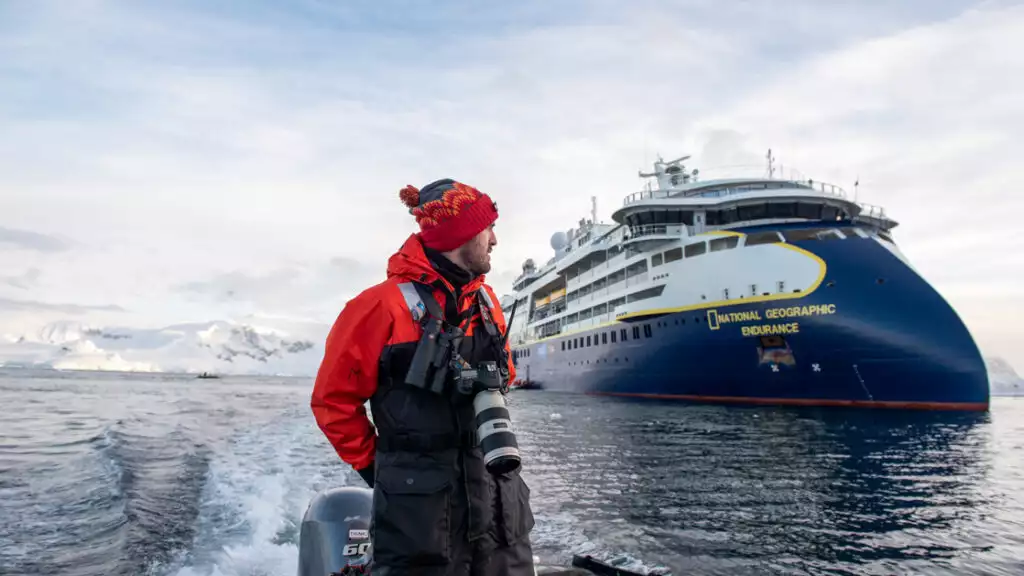 man standing on zodiac driving away from National Geographic Endurance in Foyn Harbour, Antarctica.