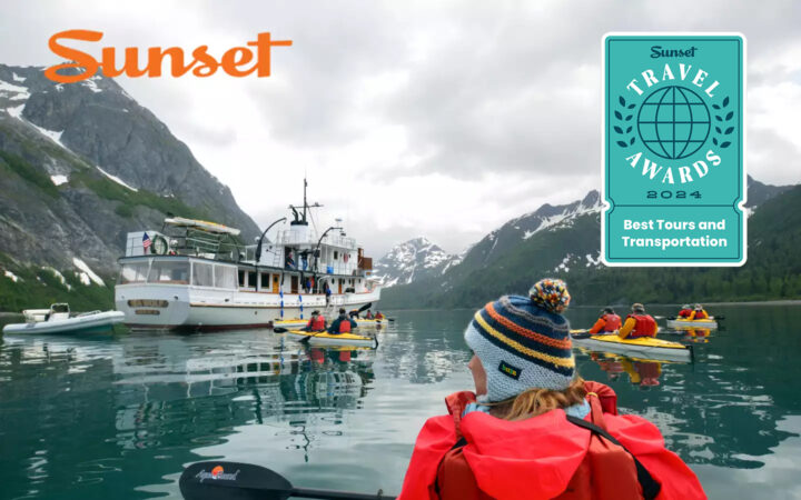 Girl wearing colorful beanie kayaking in Alaska amongst other kayakers headed towards a small white wooden ship.