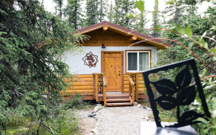 Exterior of a small, modern log cabin at Denali lodge Tonglen Lake, with window, front steps & wrought iron artwork