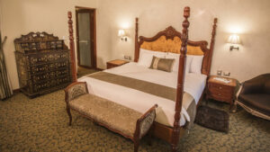 Doubled bedroom with white bed sheets and a traditional classic look with a bench at the end of the bed at Aranwa Cusco boutique