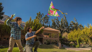Father and son fly a pink and green kite in front of the Aranwa Sacred Valley Hotel surrounded by green trees