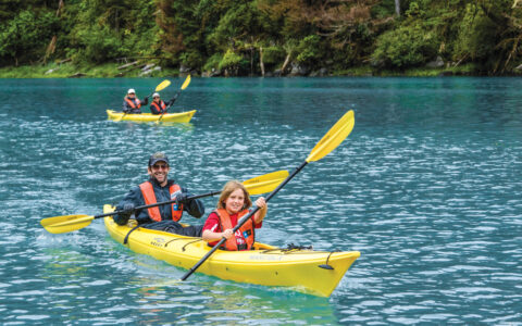 A family of four explores in yellow kayaks and red life vests in Alaska, USA