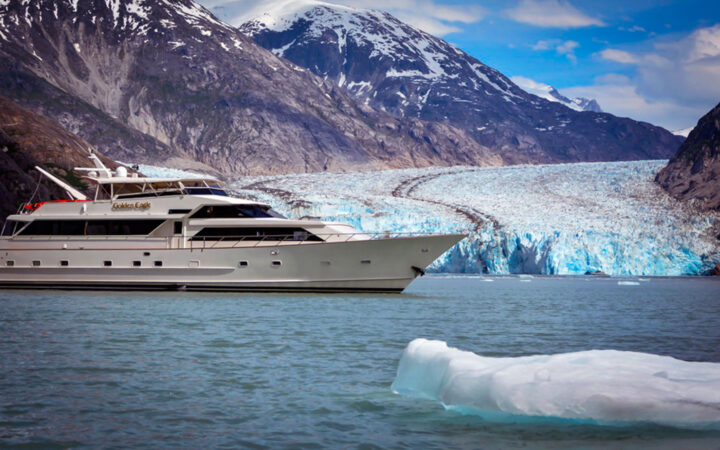 Golden Eagle yacht cruising in front of a large glacier in southeast Alaska with icebergs around the ship.