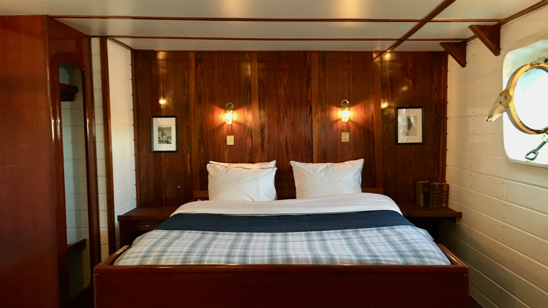 Double cabin on MS Balto with fixed double bed, wood & white walls, reading lamps & porthole.