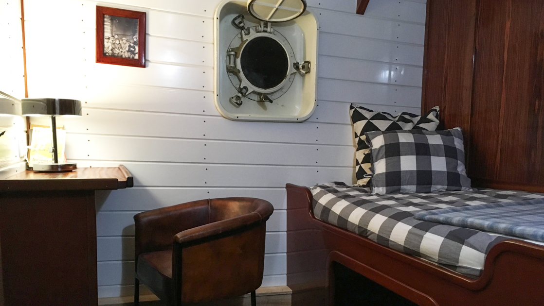 Single cabin on MS Balto with fixed twin bed, white & wood walls, portholes, small wooden desk & leather chair.