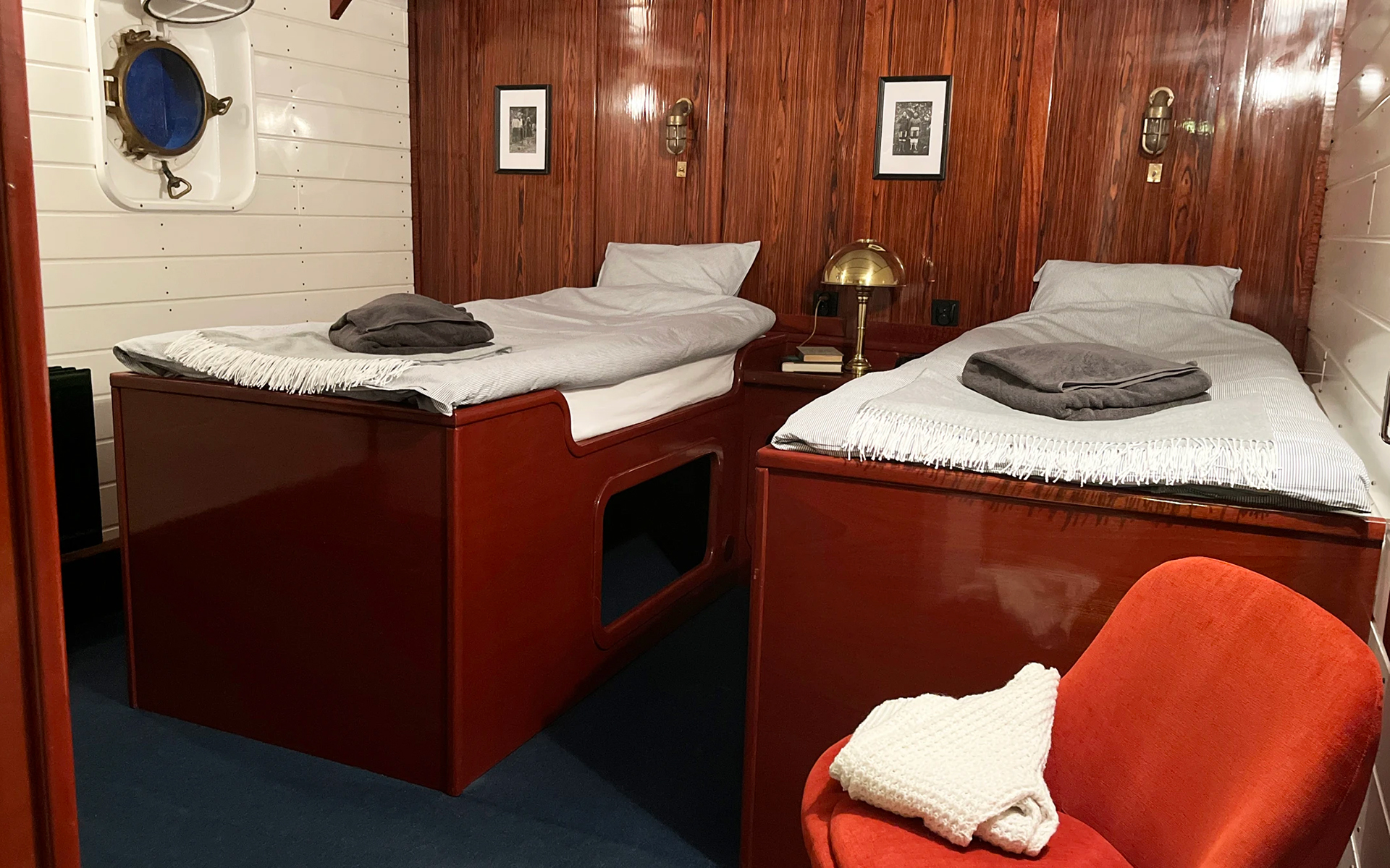 Twin cabin on MS Balto with 2 fixed twin beds, white & wood walls, 2 portholes, runner rug & leather chair.