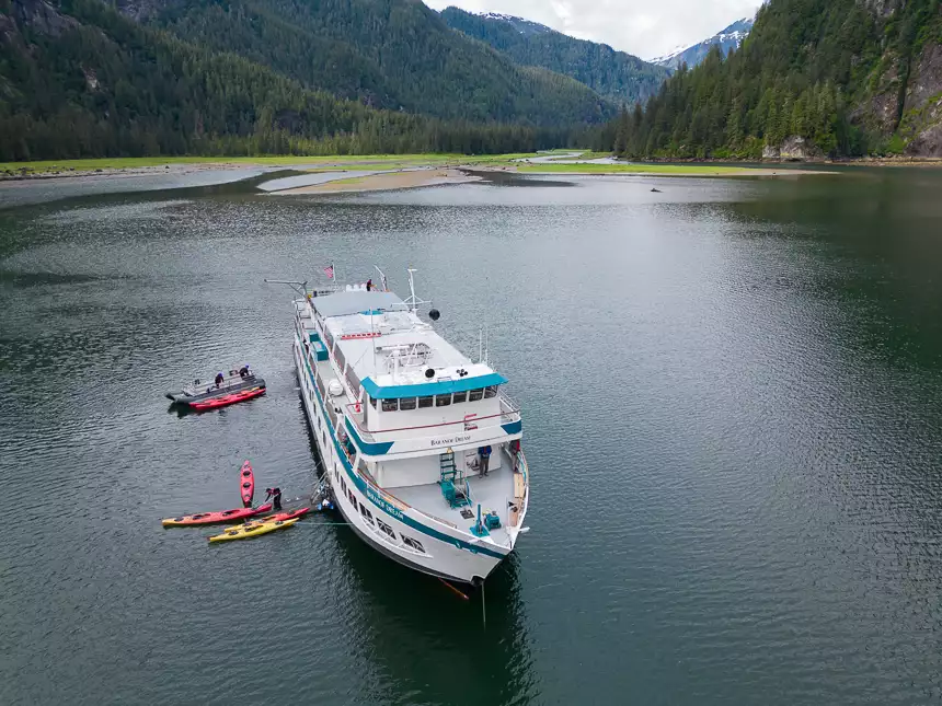 Areal drone photo of Baranof Dream ship anchored near shore as crew prepares kayaks and skiff for daily activity. 