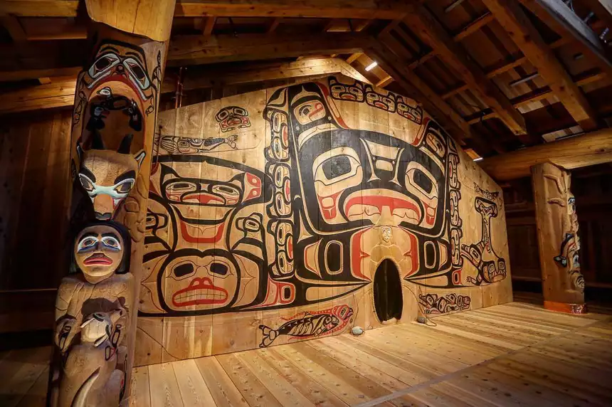 Inside a longhouse in Alaska. Wooden totem poles and wall with Indigenous art traditions with symbols or figures in black and red. 