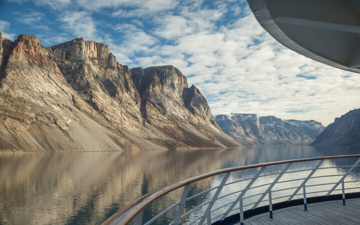View from a Northwest Passage cruise ship showing the ship railing and the still water and steep mountainsides