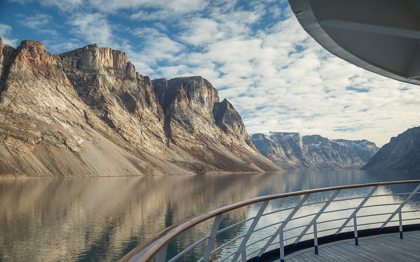 View from a Northwest Passage cruise ship showing the ship railing and the still water and steep mountainsides
